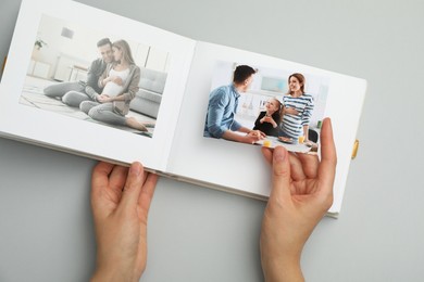 Photo of Woman with open photo album and photos on grey background, top view