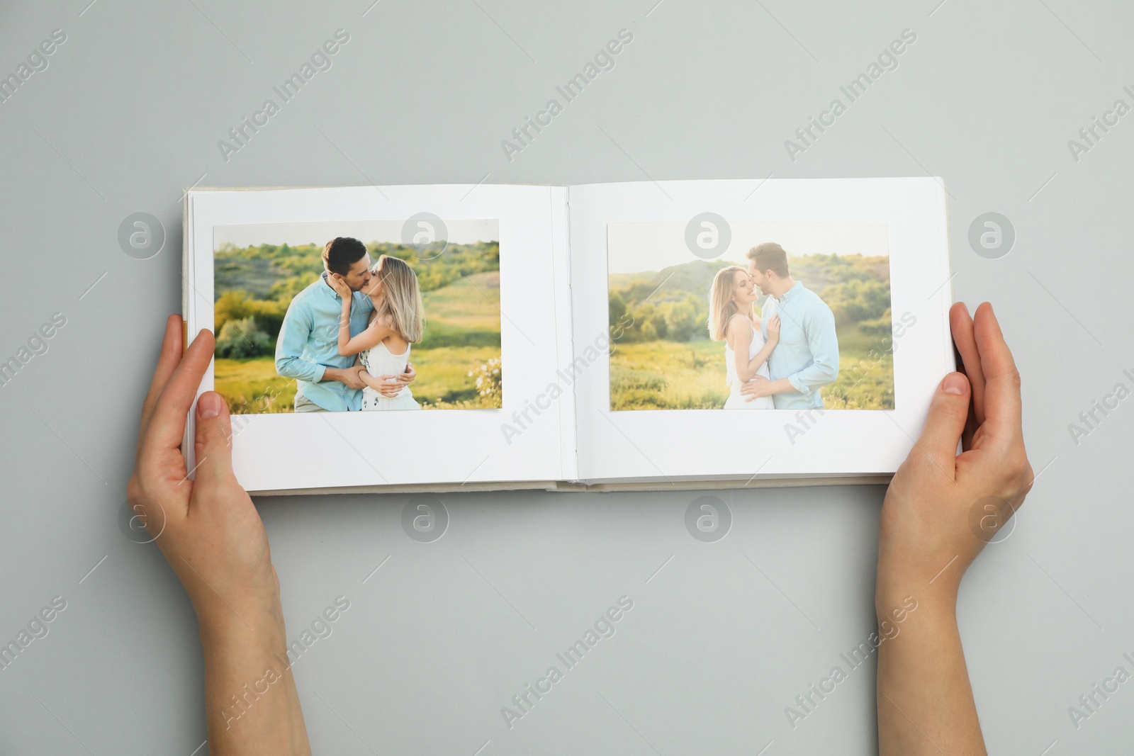 Photo of Woman looking at family photos in photo album on grey background, top view