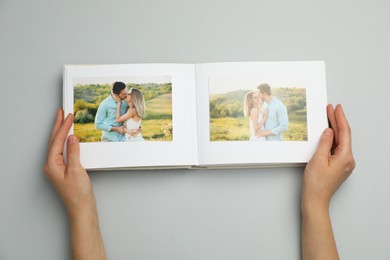 Photo of Woman looking at family photos in photo album on grey background, top view