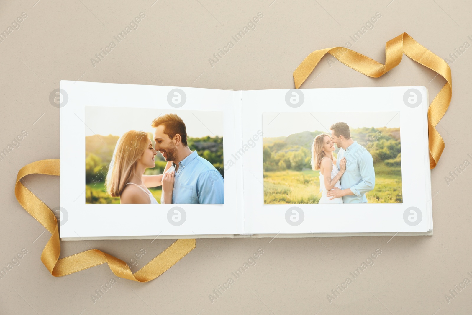 Photo of Open photo album with photos and ribbon on beige background, top view