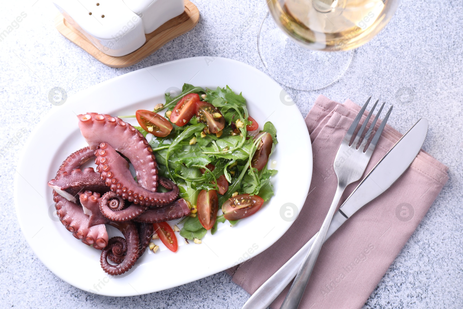 Photo of Plate with tasty boiled octopus tentacles and salad served on grey textured table, flat lay