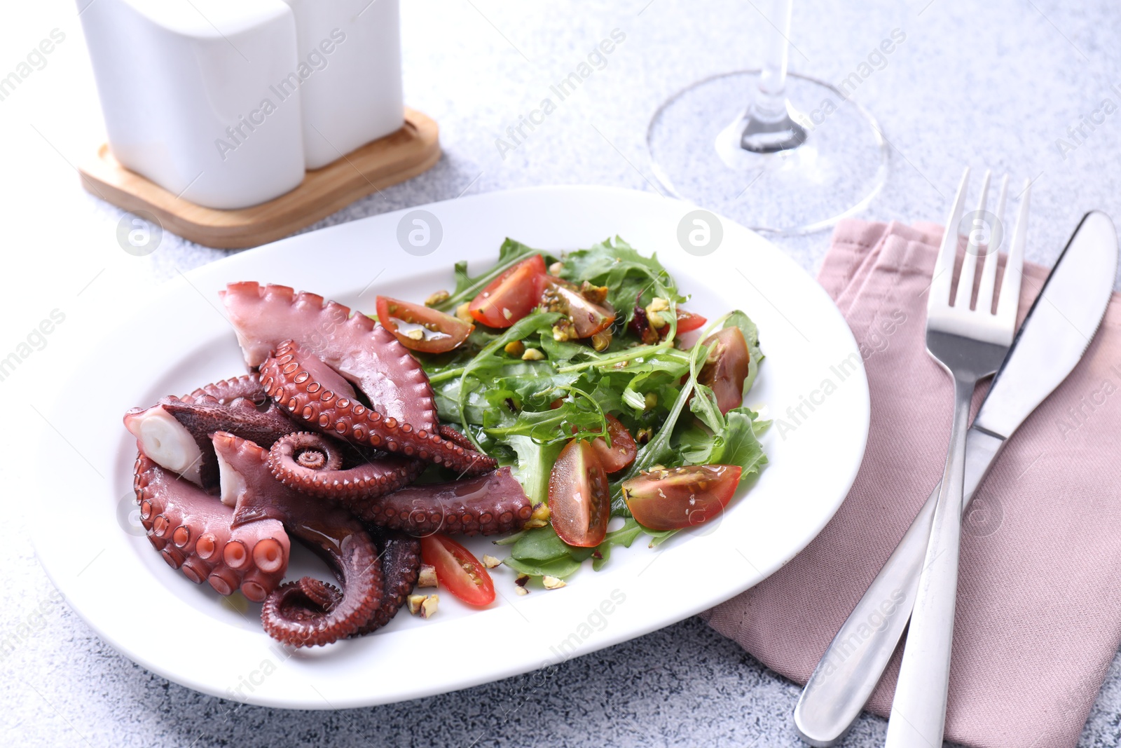 Photo of Plate with tasty boiled octopus tentacles and salad served on grey textured table, closeup