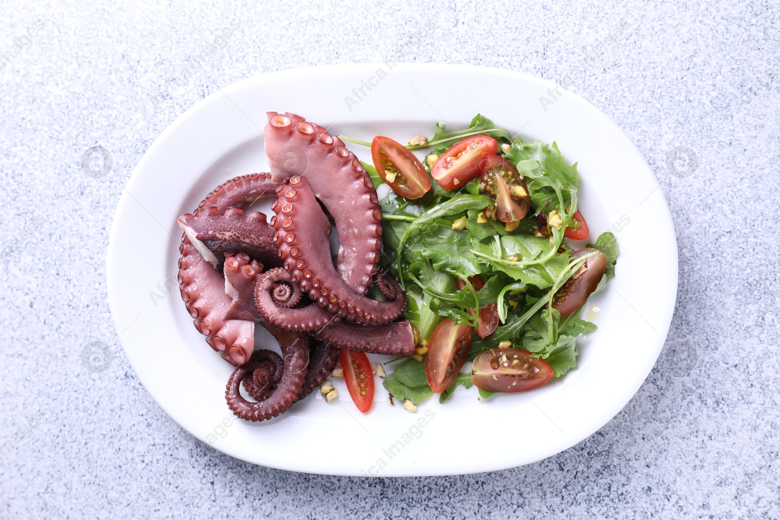 Photo of Plate with tasty boiled octopus tentacles and salad on grey textured table, top view