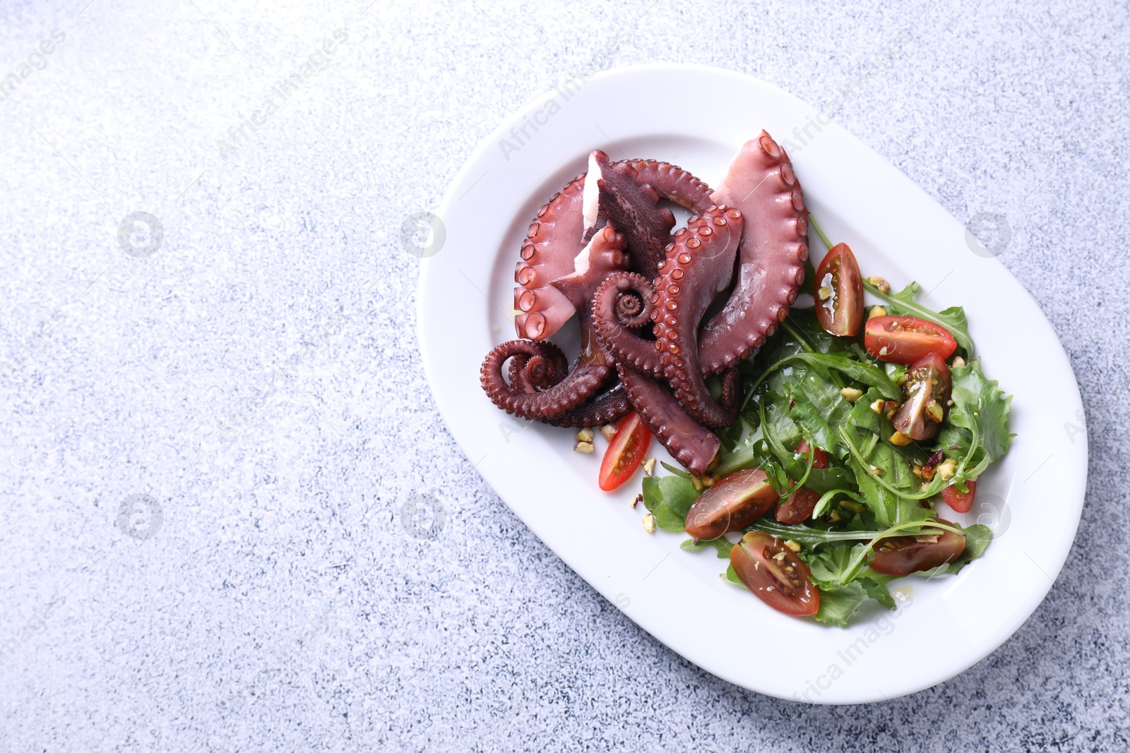 Photo of Plate with tasty boiled octopus tentacles and salad on grey textured table, top view. Space for text