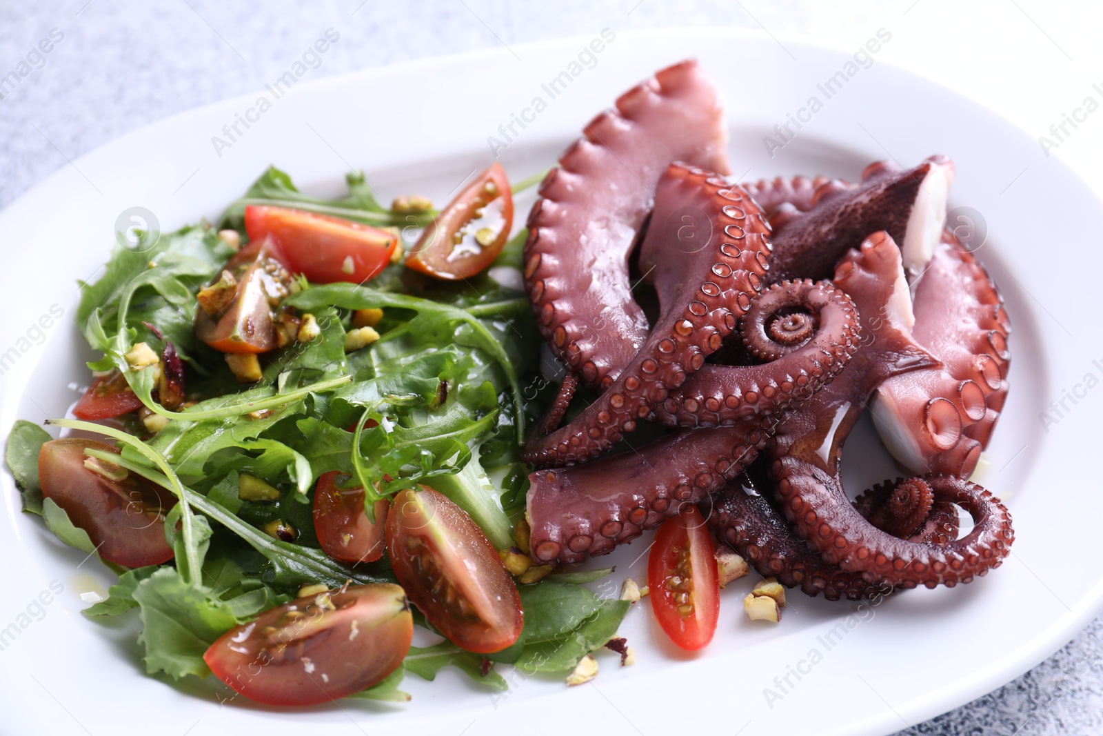 Photo of Plate with tasty boiled octopus tentacles and salad on table, closeup