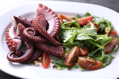 Photo of Plate with tasty boiled octopus tentacles and salad on table, closeup