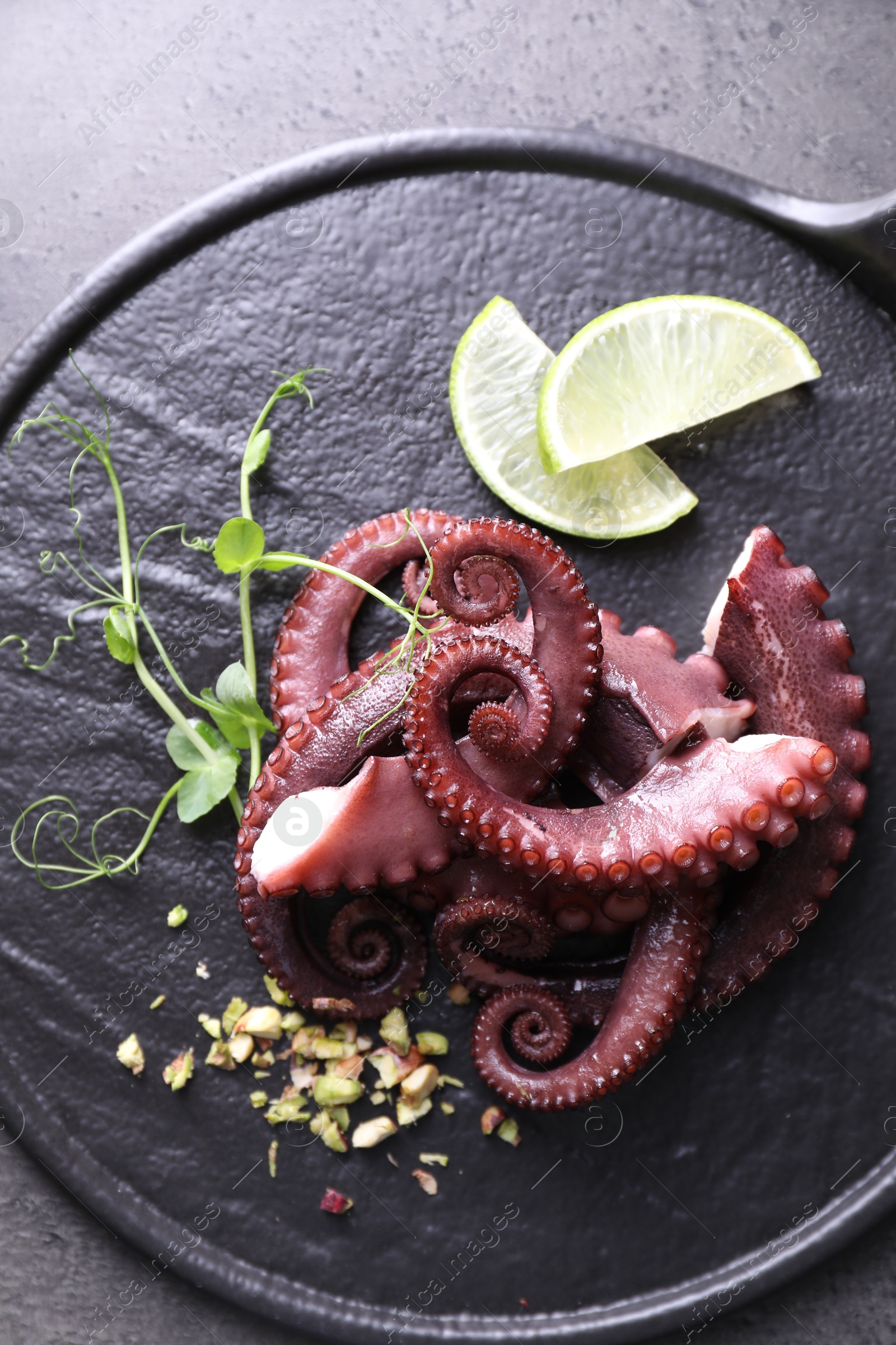 Photo of Tasty boiled octopus tentacles, microgreens, nuts and lime on grey table, top view