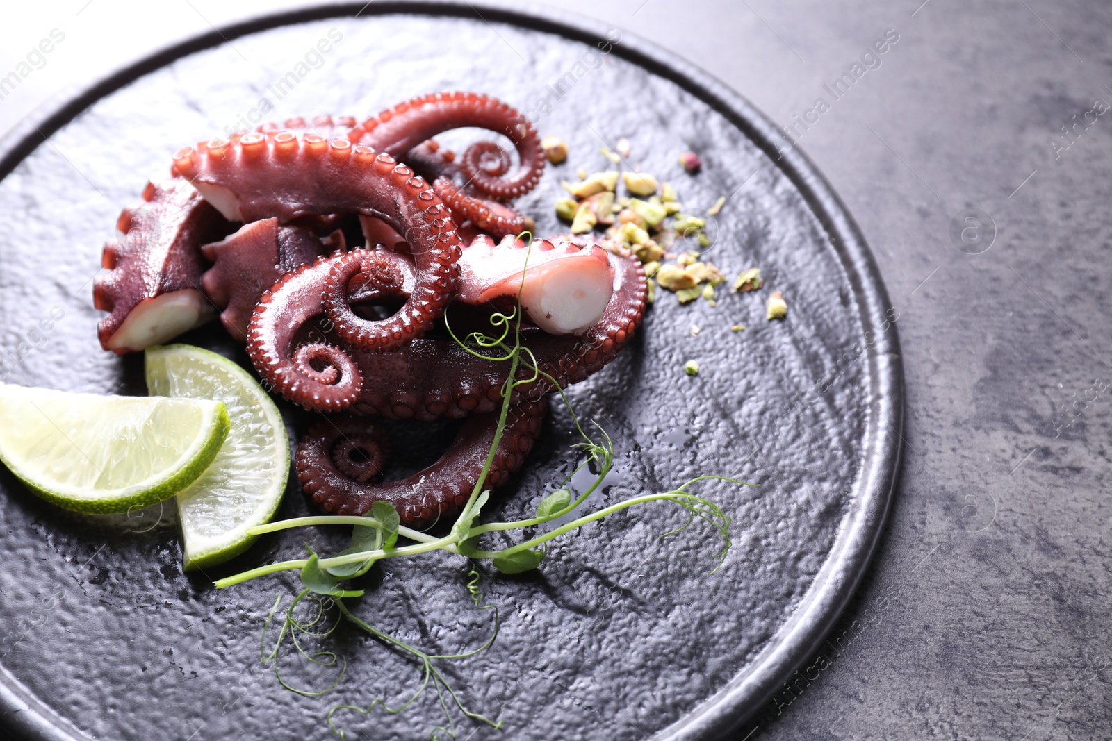 Photo of Tasty boiled octopus tentacles, microgreens, nuts and lime on grey table, closeup