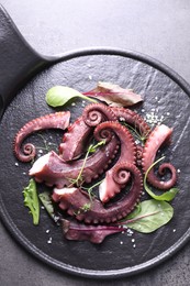 Photo of Tasty boiled octopus tentacles, microgreens and salt on grey textured table, top view.