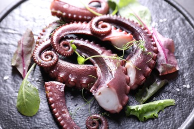 Photo of Tasty boiled octopus tentacles and microgreens on grey table, closeup