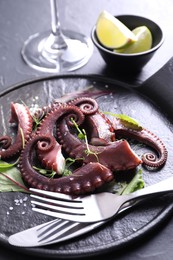 Photo of Tasty boiled octopus tentacles, microgreens, salt and cutlery on grey table, closeup