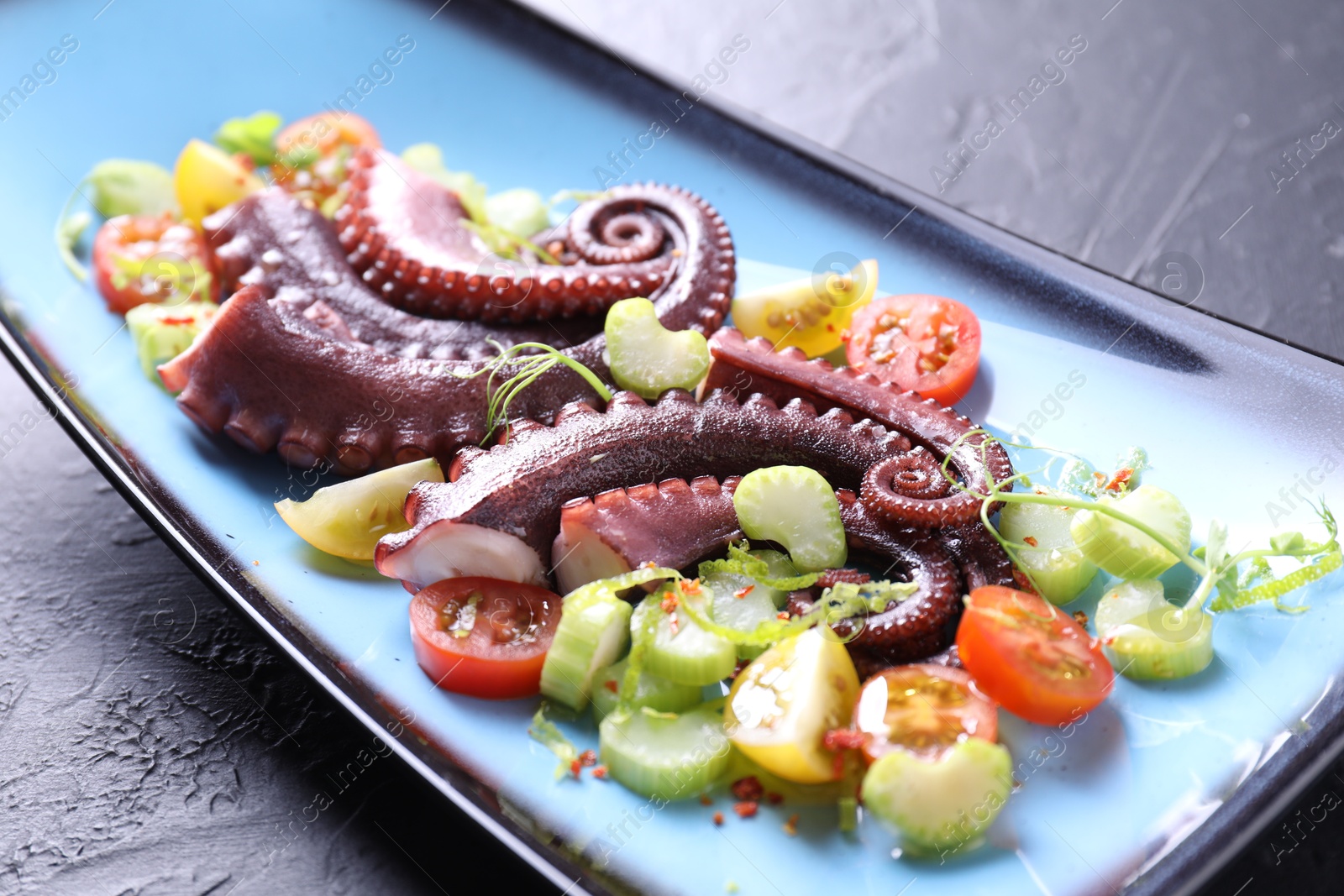 Photo of Tasty boiled octopus tentacles and salad on grey textured table, closeup