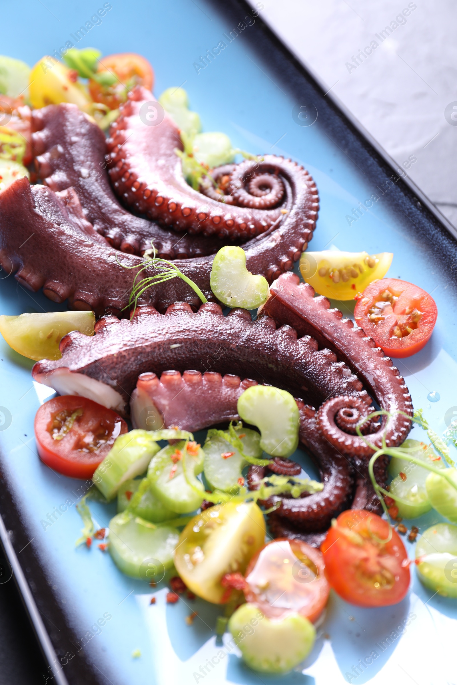 Photo of Tasty boiled octopus tentacles and salad on grey table, closeup