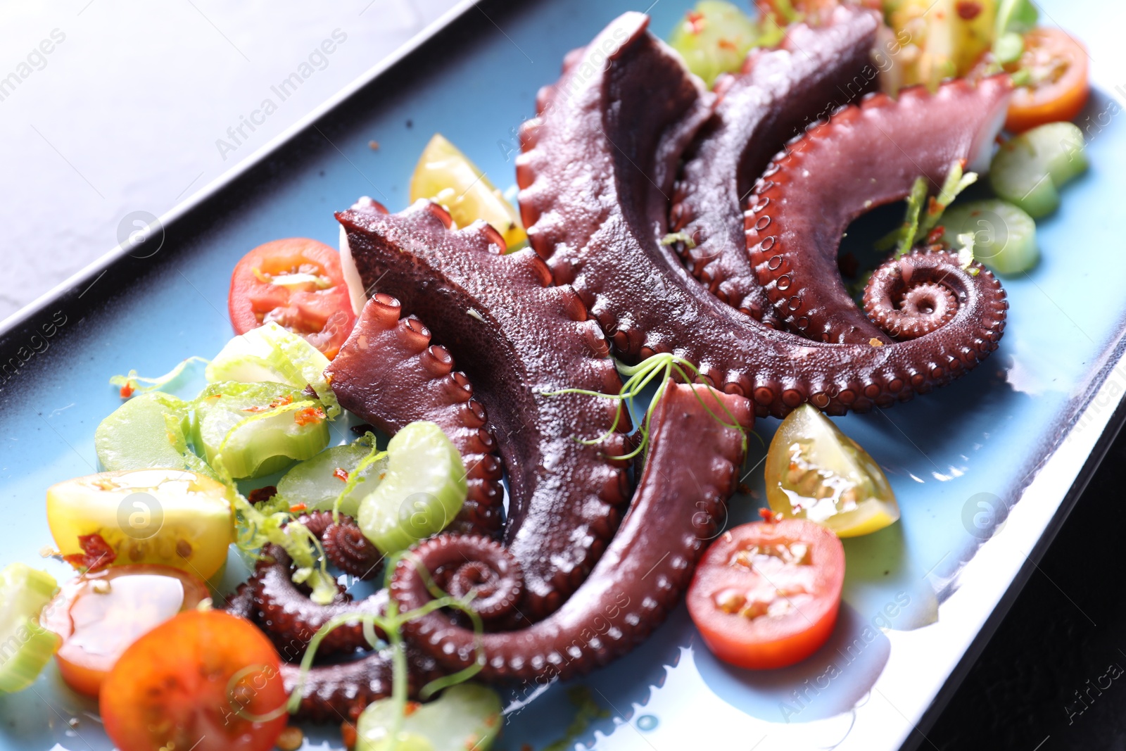 Photo of Tasty boiled octopus tentacles and salad on grey table, closeup