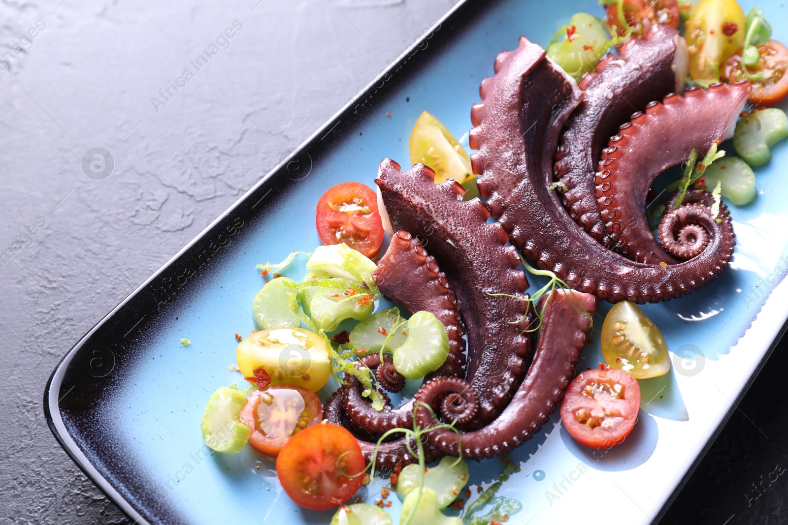 Photo of Tasty boiled octopus tentacles and salad on grey textured table, closeup