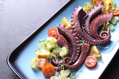 Photo of Tasty boiled octopus tentacles and salad on grey textured table, closeup