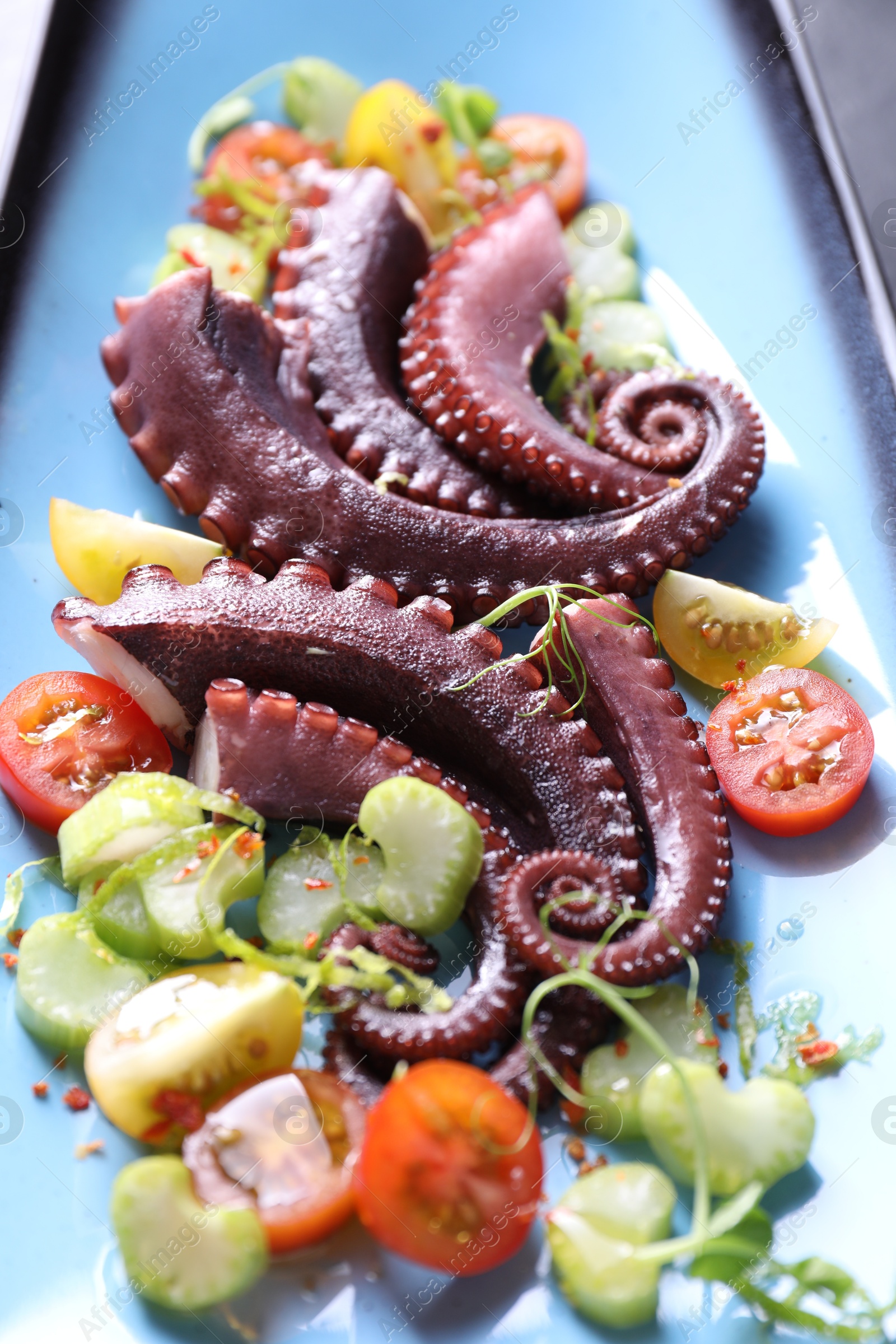 Photo of Tasty boiled octopus tentacles and salad on grey table, closeup