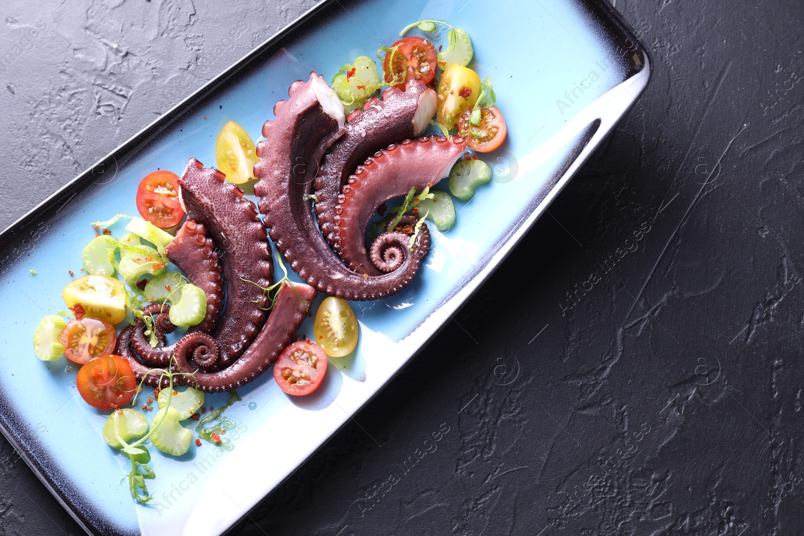 Photo of Tasty boiled octopus tentacles and salad on grey textured table, top view. Space for text