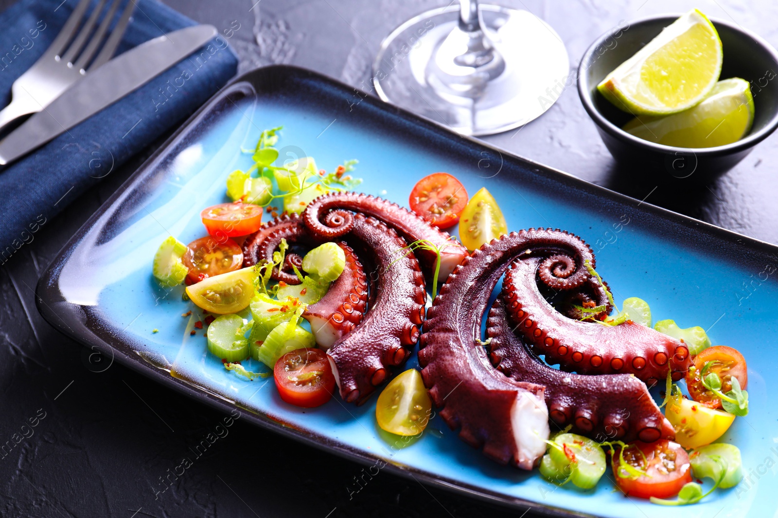 Photo of Tasty boiled octopus tentacles and salad served on grey textured table, closeup