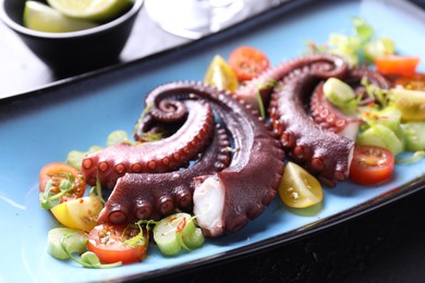 Photo of Tasty boiled octopus tentacles and salad on table, closeup