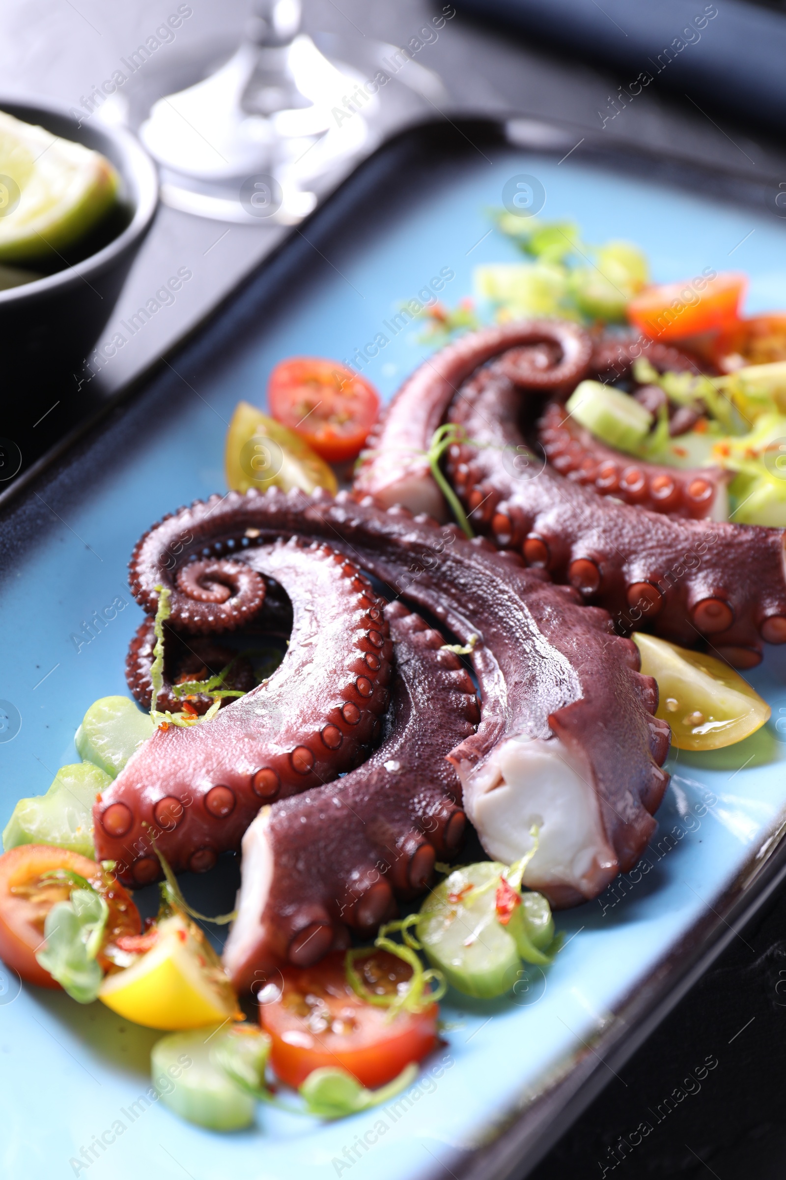 Photo of Tasty boiled octopus tentacles and salad on table, closeup