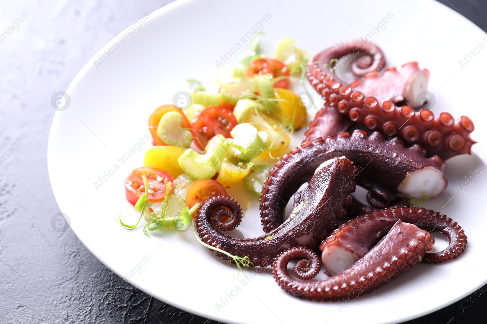 Photo of Plate with tasty boiled octopus tentacles and salad on grey textured table, closeup