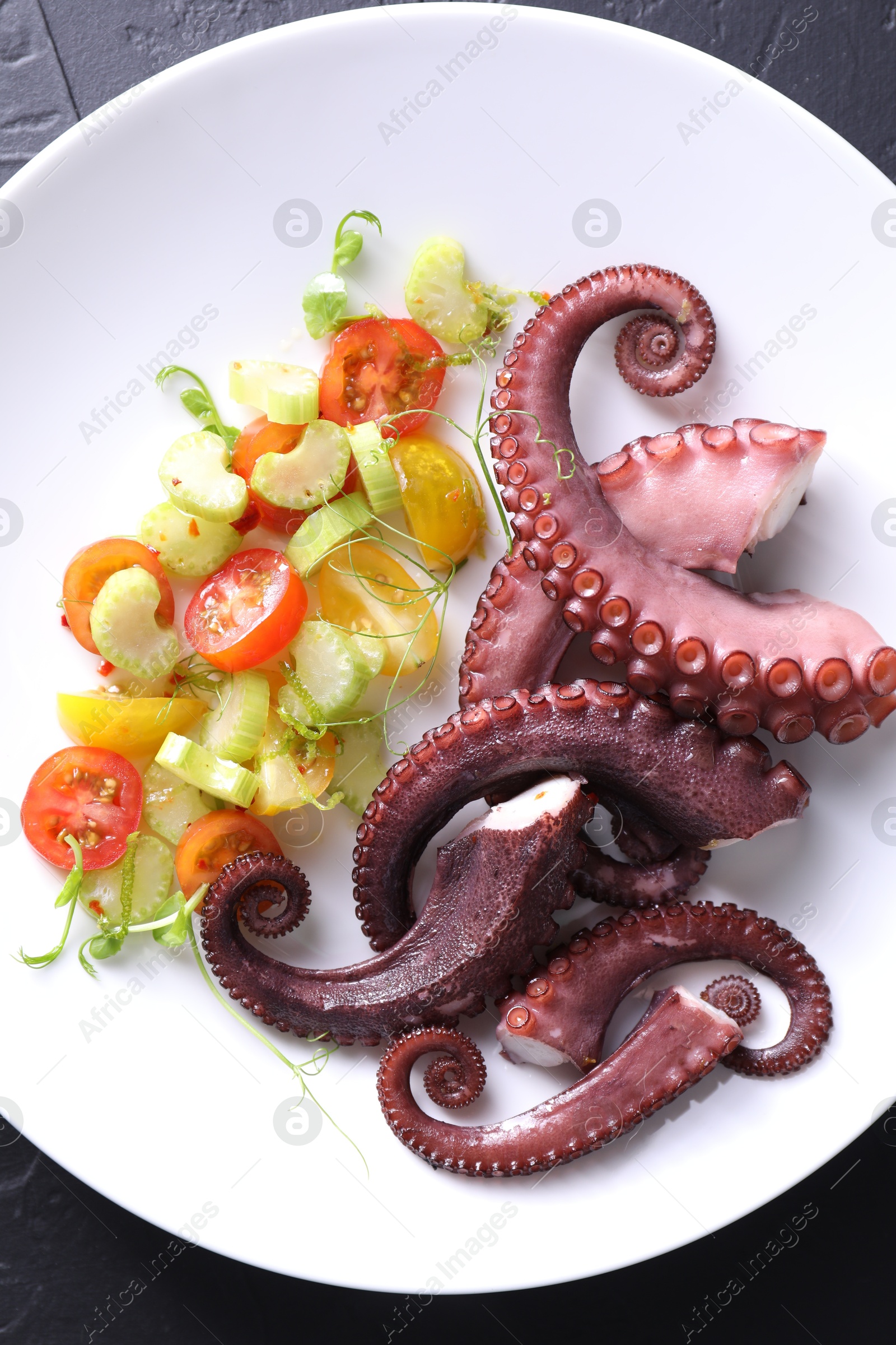 Photo of Plate with tasty boiled octopus tentacles and salad on grey textured table, top view