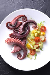 Plate with tasty boiled octopus tentacles and salad on grey textured table, top view