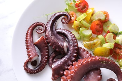 Plate with tasty boiled octopus tentacles and salad on white table, top view