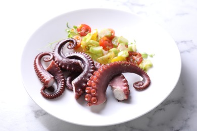 Photo of Plate with tasty boiled octopus tentacles and salad on white marble table, closeup