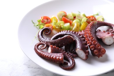 Plate with tasty boiled octopus tentacles and salad on white marble table, closeup