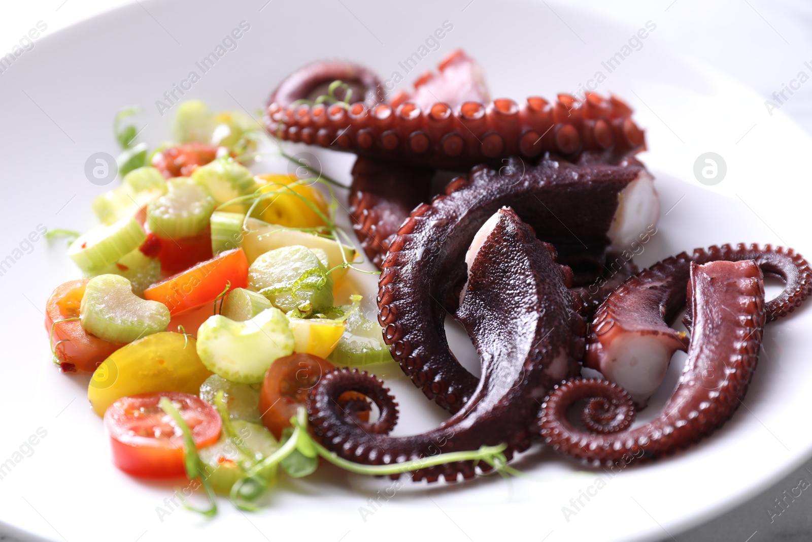 Photo of Tasty boiled octopus tentacles and salad on plate, closeup