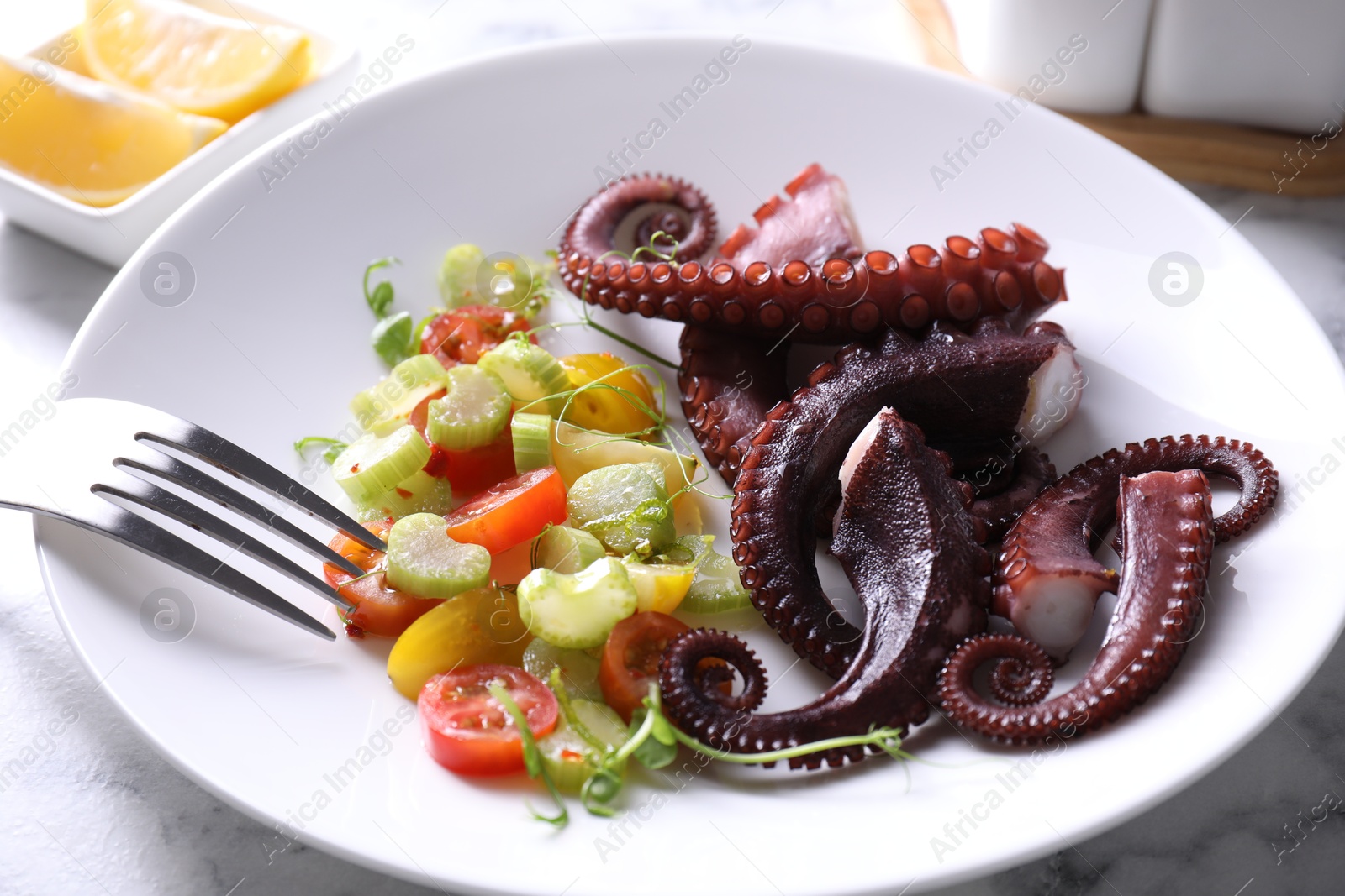 Photo of Plate with tasty boiled octopus tentacles, salad and fork on white marble table, closeup