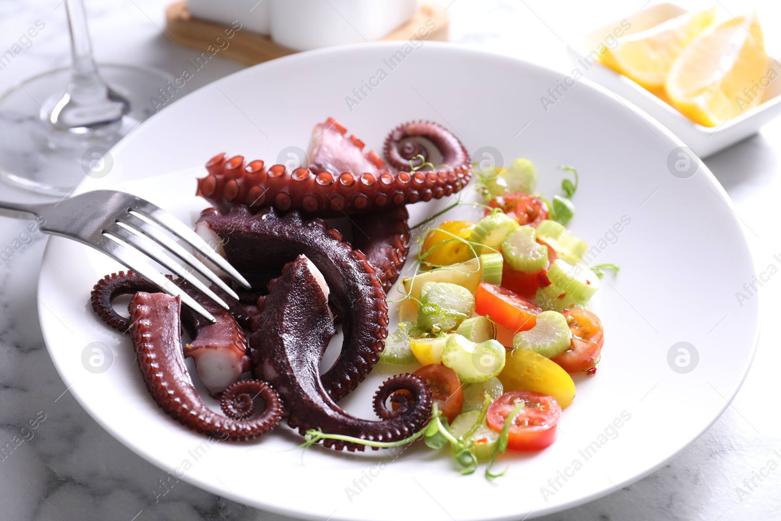 Photo of Plate with tasty boiled octopus tentacles, salad and fork on white marble table, closeup