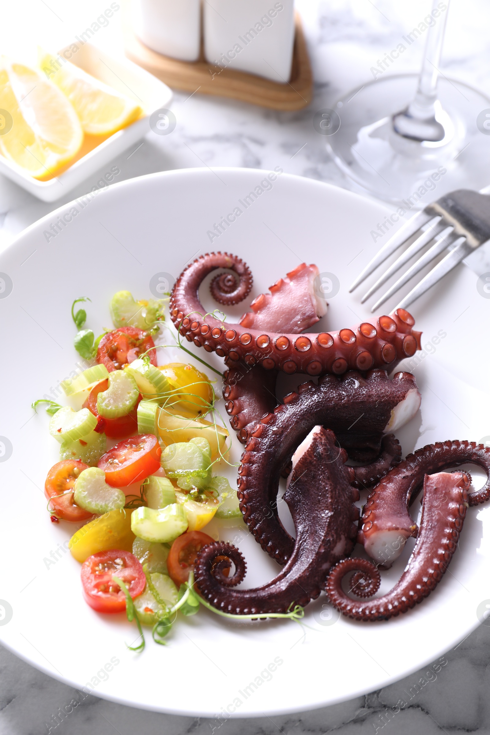 Photo of Plate with tasty boiled octopus tentacles, salad and fork on white marble table, above view