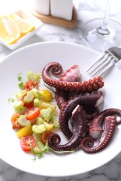 Photo of Plate with tasty boiled octopus tentacles, salad and fork on white marble table, above view