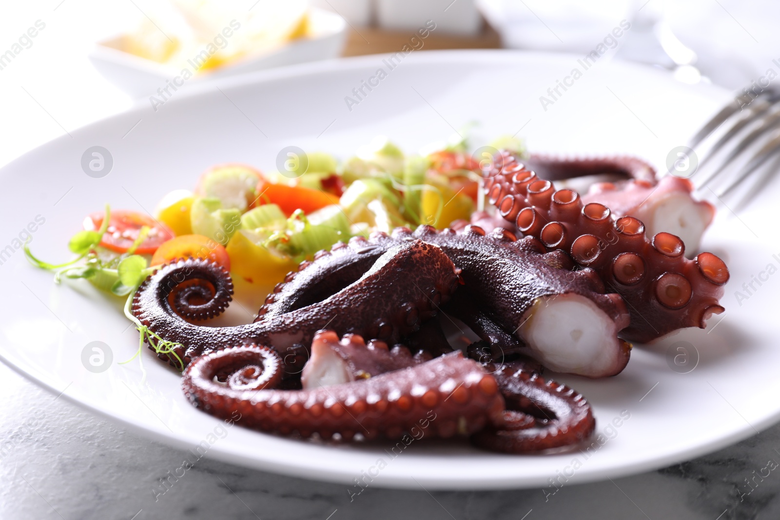 Photo of Plate with tasty boiled octopus tentacles and salad on white table, closeup