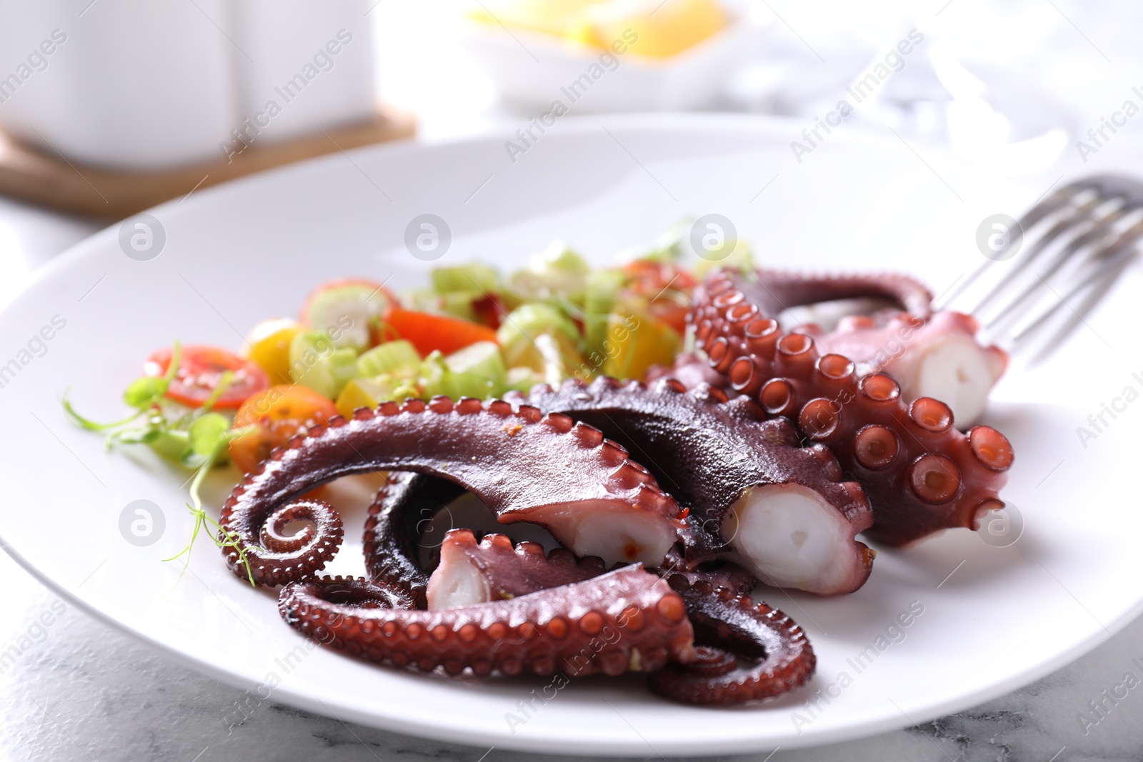 Photo of Plate with tasty boiled octopus tentacles and salad on white table, closeup