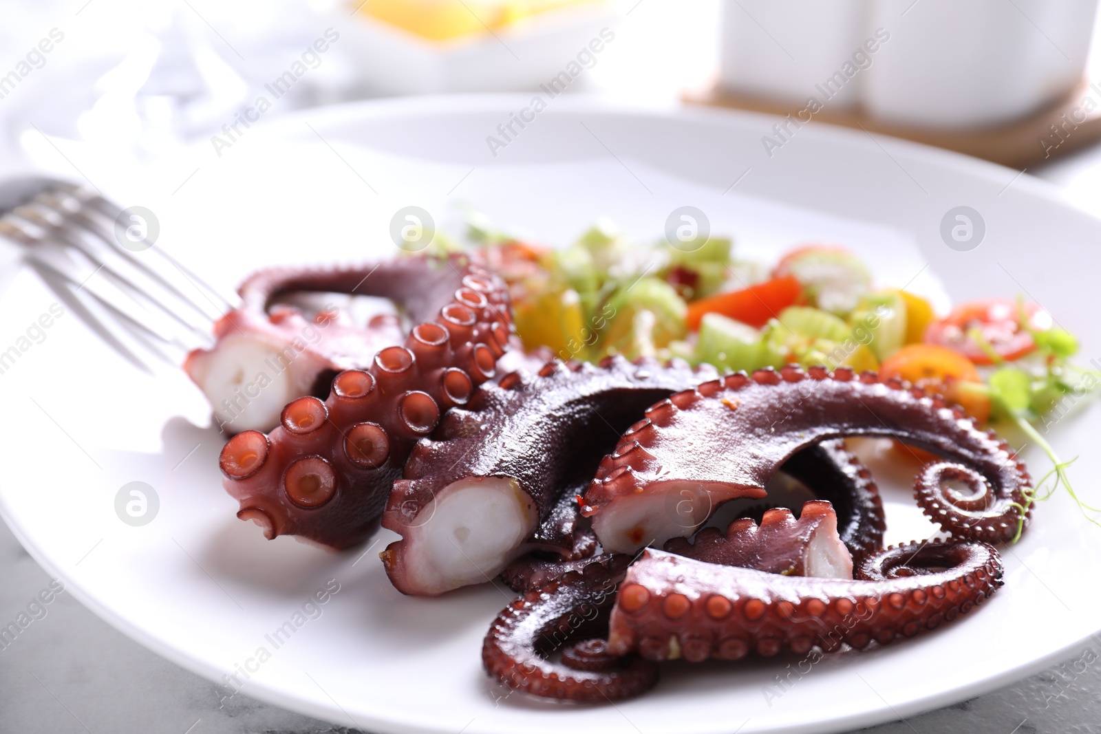 Photo of Plate with tasty boiled octopus tentacles and salad on white table, closeup