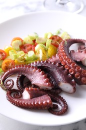 Photo of Plate with tasty boiled octopus tentacles and salad on light table, closeup