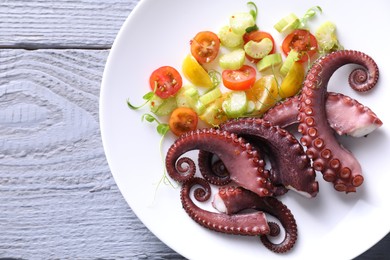 Photo of Plate with tasty boiled octopus tentacles and salad on grey wooden table, top view. Space for text