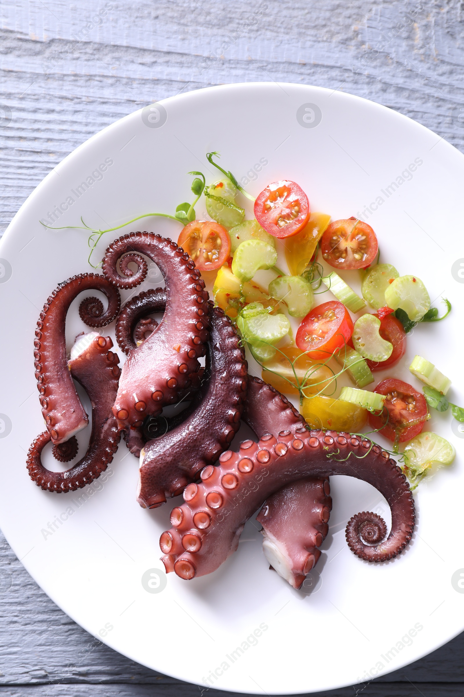 Photo of Plate with tasty boiled octopus tentacles and salad on grey wooden table, top view