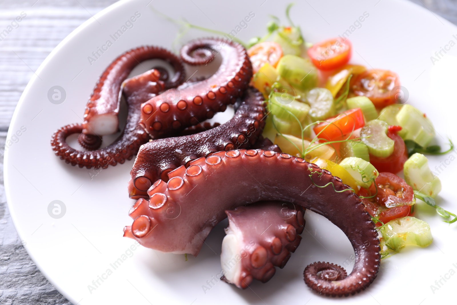 Photo of Plate with tasty boiled octopus tentacles and salad on grey wooden table, closeup