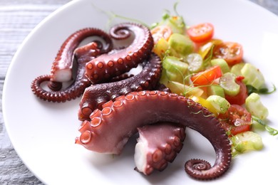 Photo of Plate with tasty boiled octopus tentacles and salad on grey wooden table, closeup