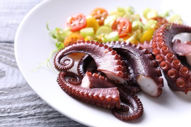 Plate with tasty boiled octopus tentacles and salad on grey wooden table, closeup