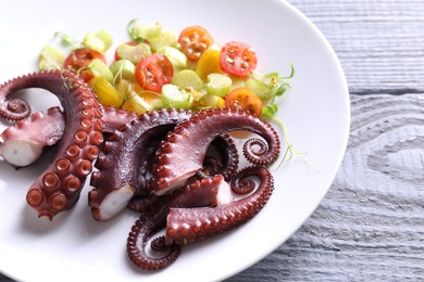 Plate with tasty boiled octopus tentacles and salad on grey wooden table, closeup