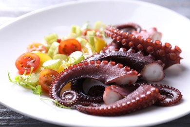 Photo of Plate with tasty boiled octopus tentacles and salad on table, closeup