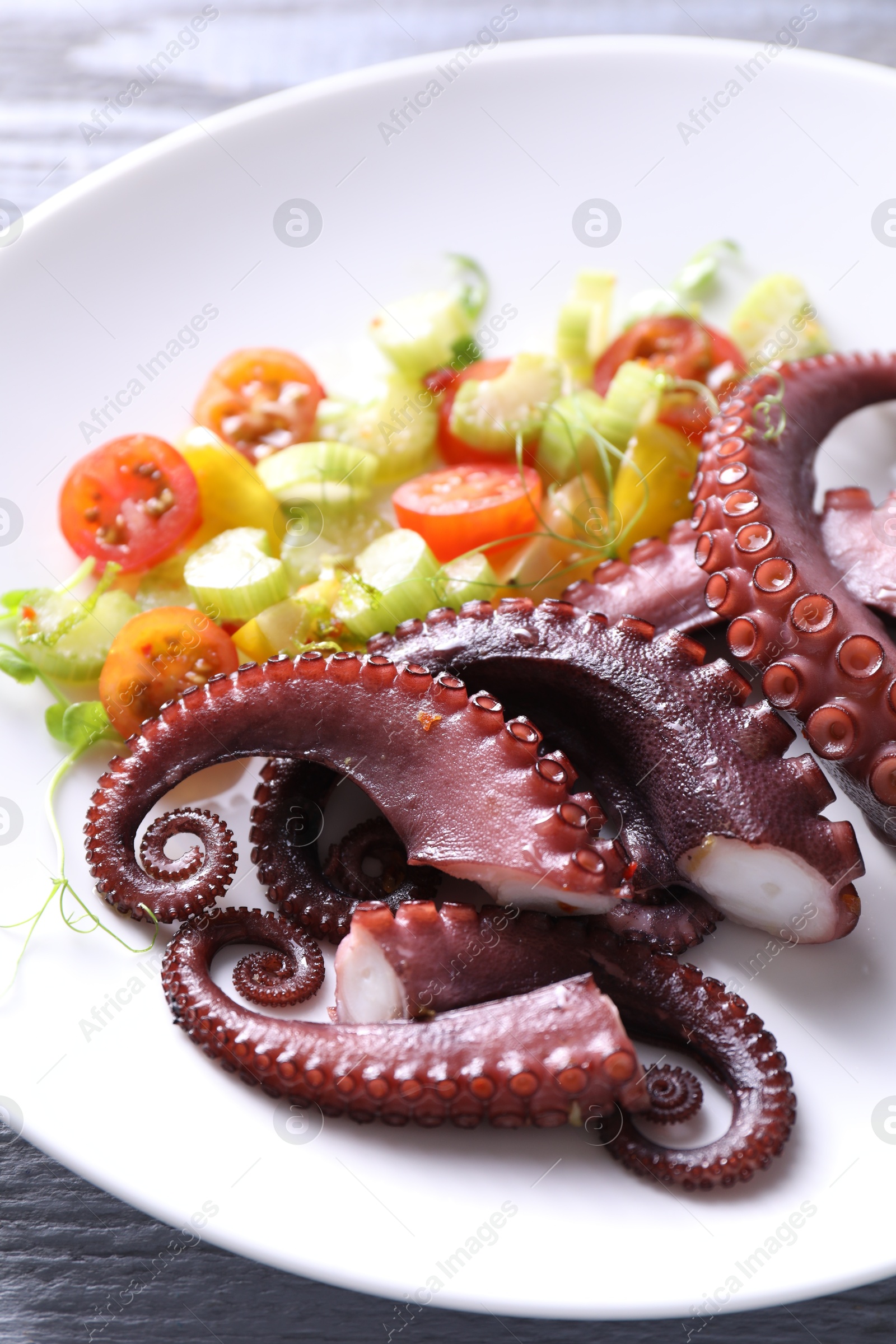 Photo of Plate with tasty boiled octopus tentacles and salad on grey wooden table, closeup