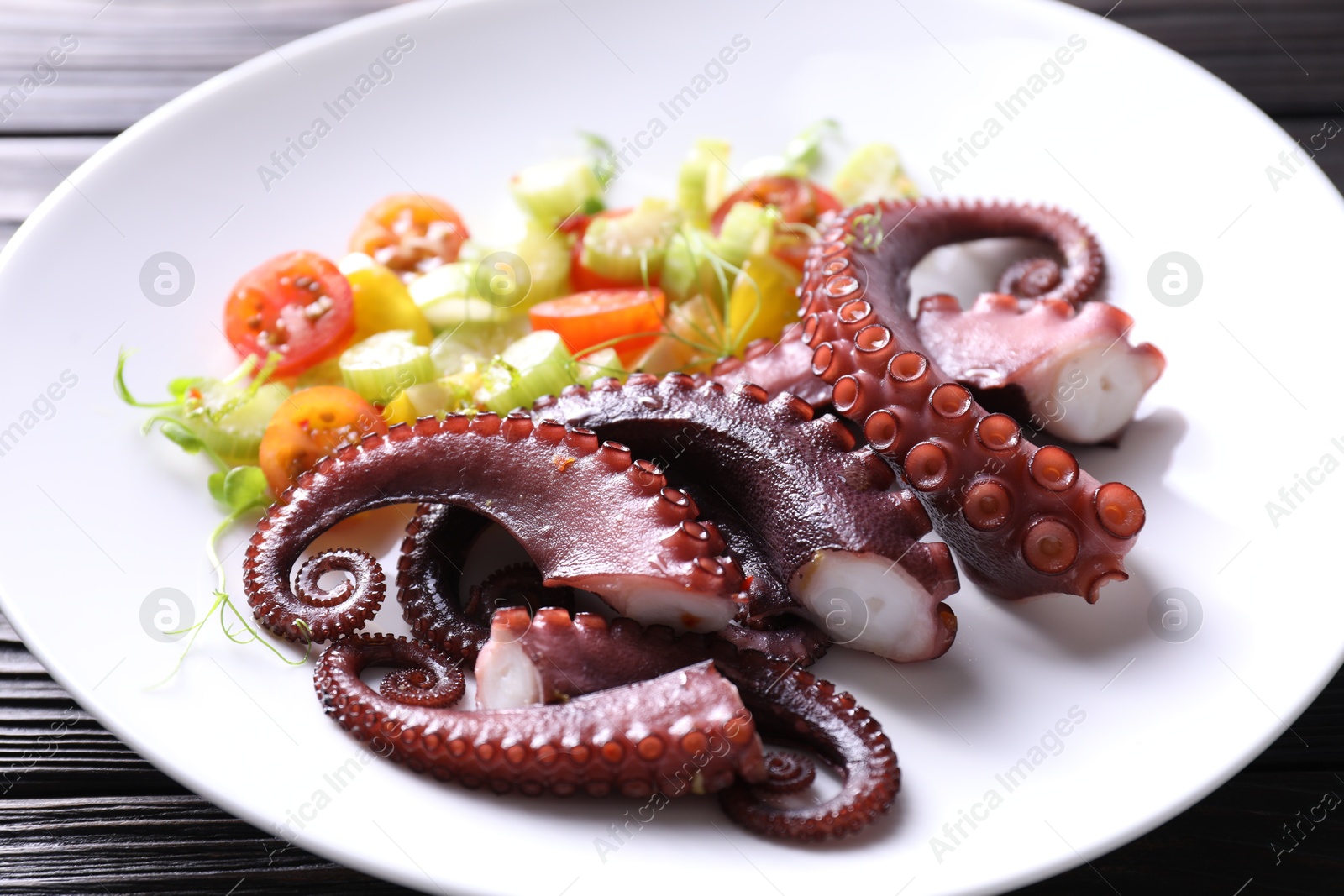 Photo of Plate with tasty boiled octopus tentacles and salad on wooden table, closeup