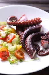 Photo of Plate with tasty boiled octopus tentacles and salad on table, closeup